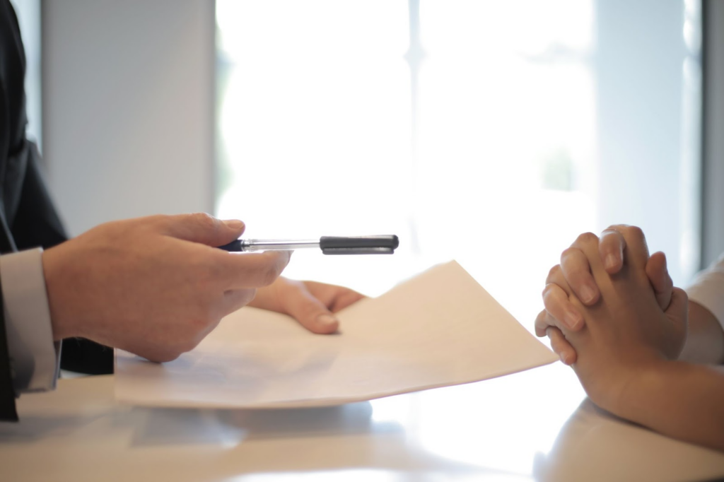 person handing pen and documents to sign to another person
